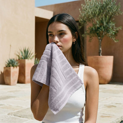 Lilac cotton towel with a textured border, folded in the hands of a person.