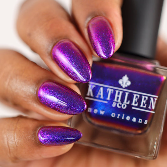 Iridescent nail polish bottle and purple-blue metallic manicured nails on fingers