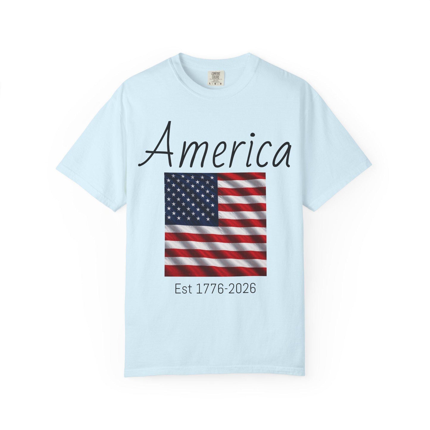 Light blue T-shirt with “America” script, USA flag graphic, and “Est 1776-2026” text