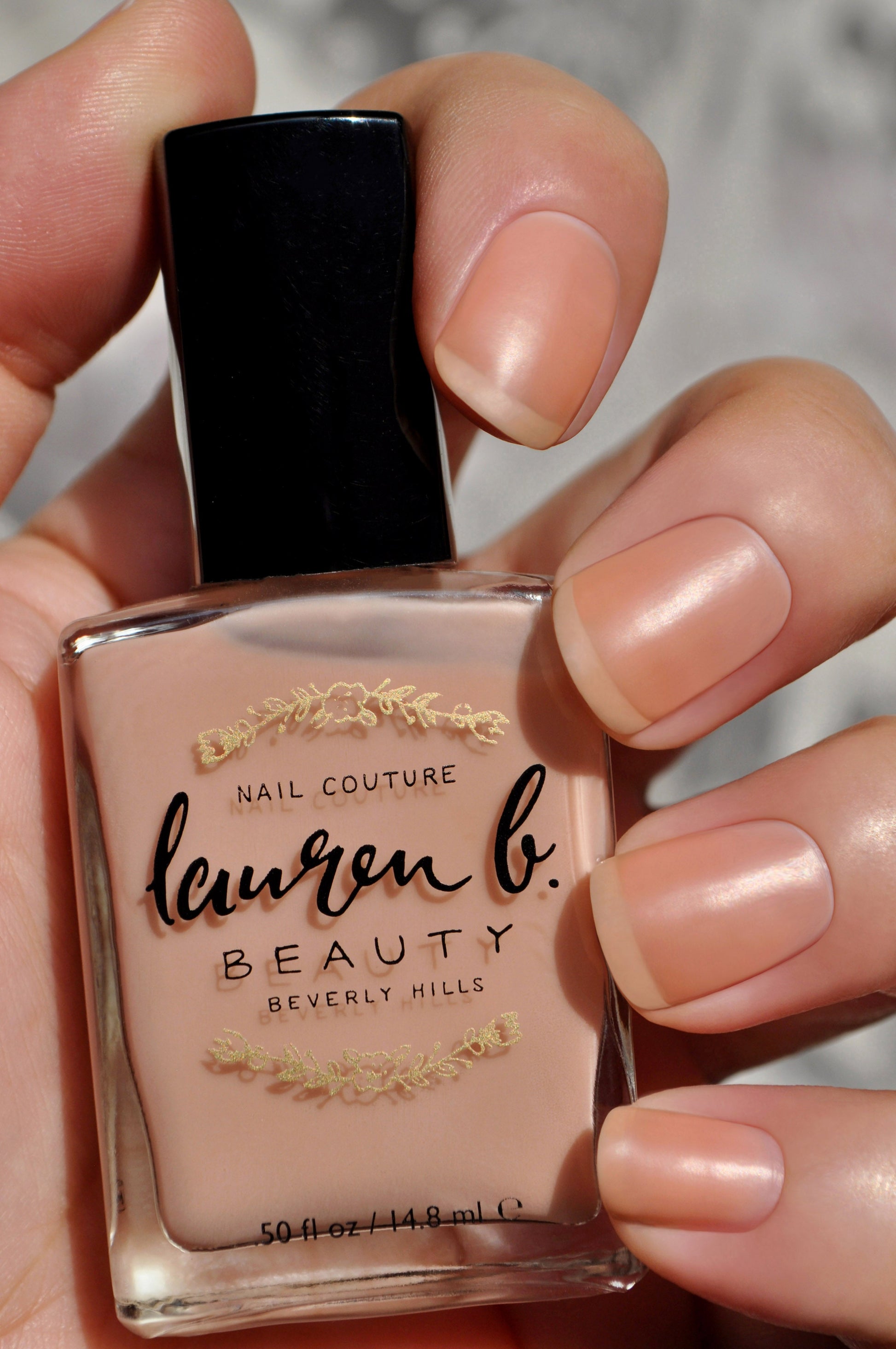 Nail base coat bottle in a nude peach shade held by fingers.
