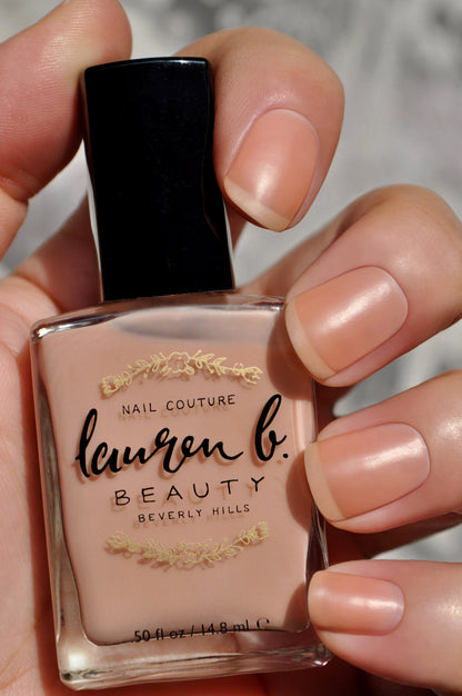 Nail base coat bottle in a nude peach shade held by fingers.