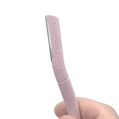 Pink speckled eyebrow razor with angled comb edge, held in a fingertip grip.