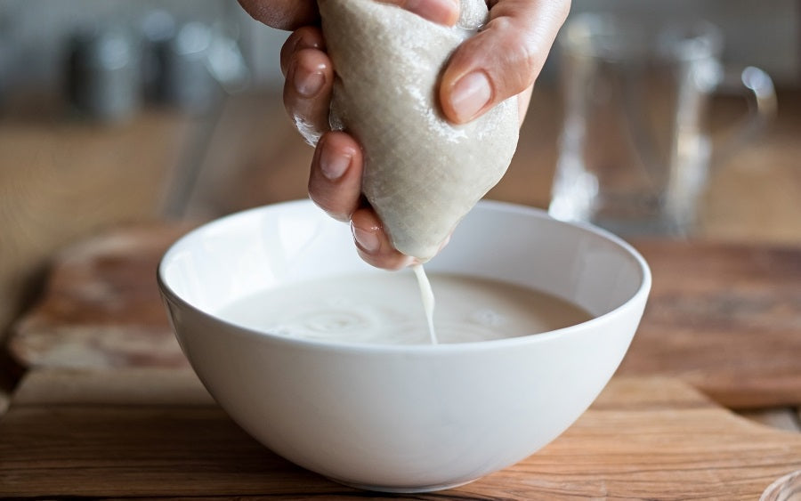 Nut milk bag being squeezed, off-white mesh pouch with drawstring