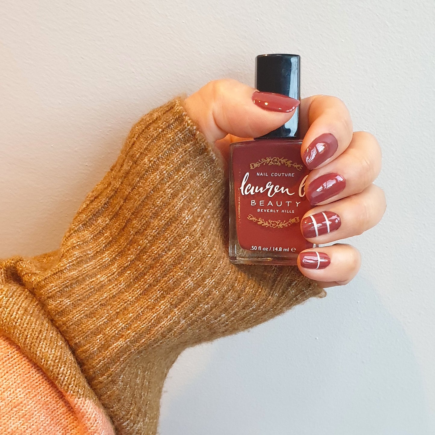 Nail polish on fingernails: deep red with white stripe accents, holding red bottle