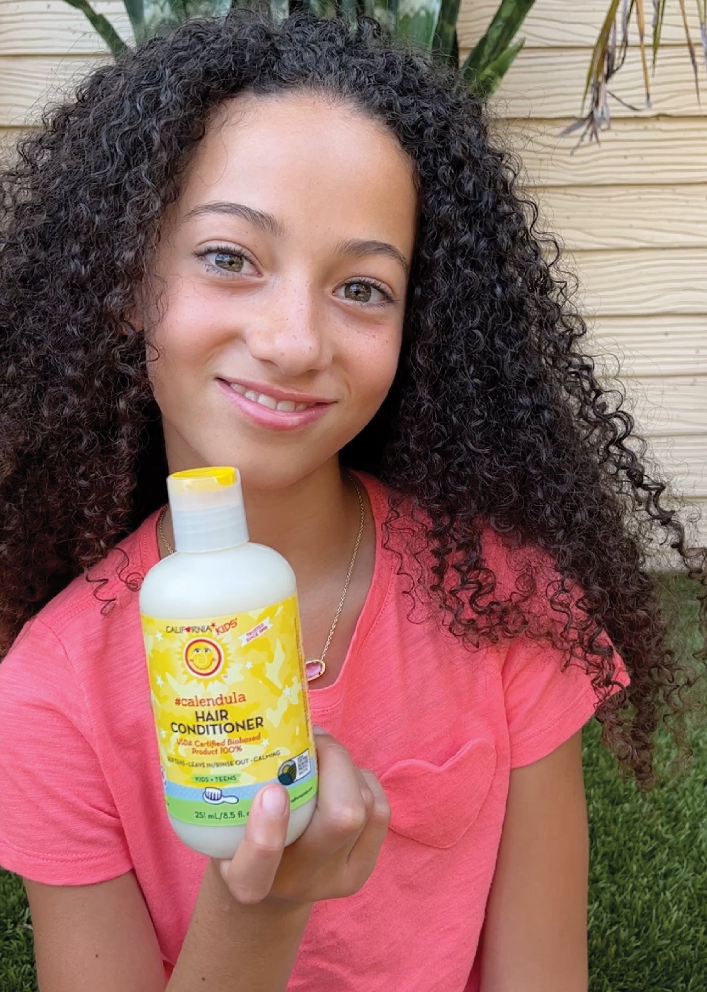 Kids Calendula hair conditioner bottle held in hand, yellow label
