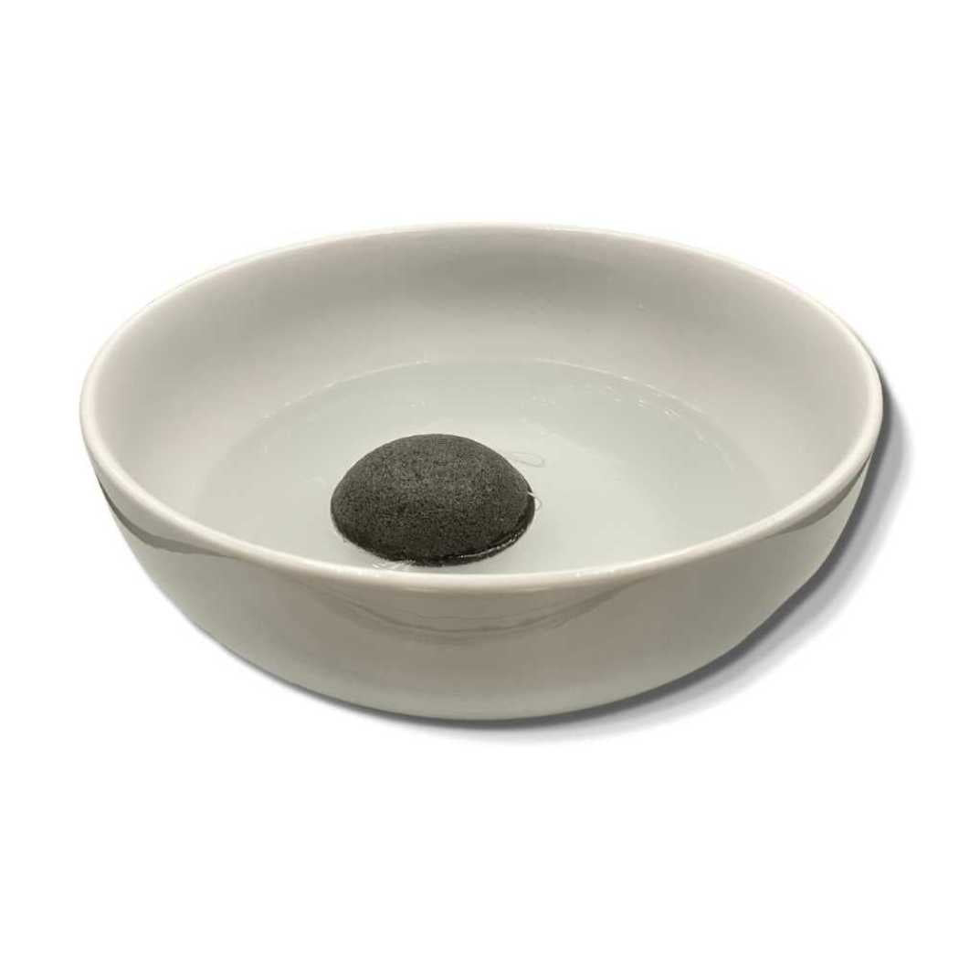 Konjac facial sponge in a shallow white bowl, dark gray.