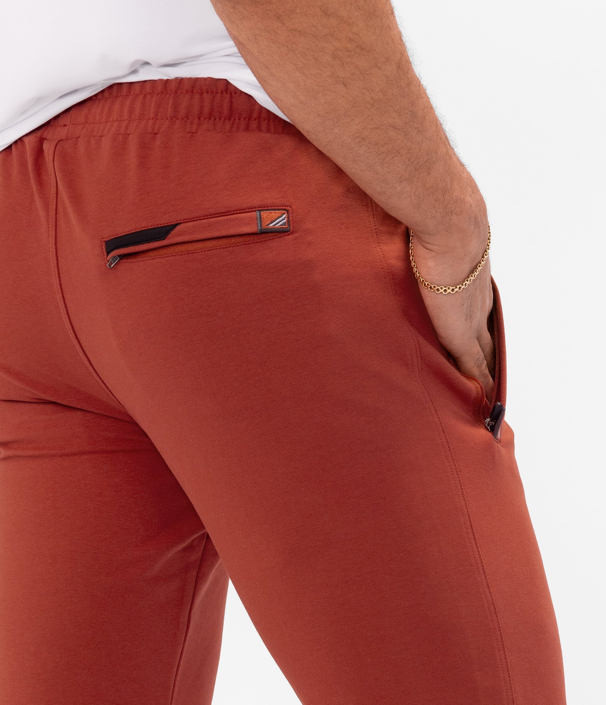 Rust red athletic sweatpants close-up: side pocket opening, drawstring, elastic waistband.