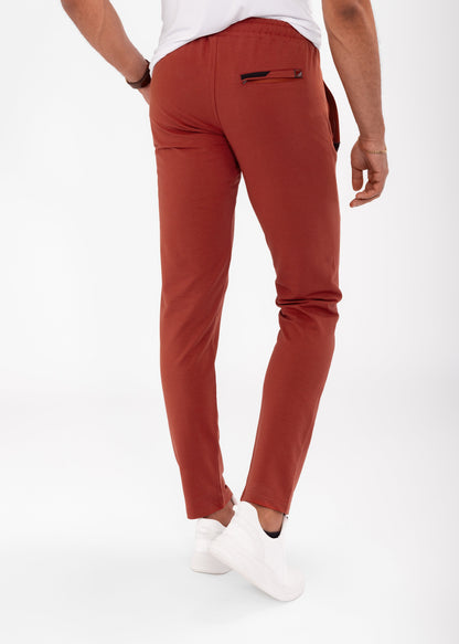 Tapered athletic sweatpants in rust red, slim leg with cuffed hem, side pocket detail.