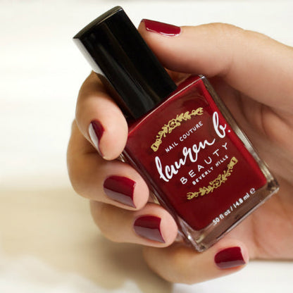 Burgundy nail polish bottle held by hand with matching manicured nails.