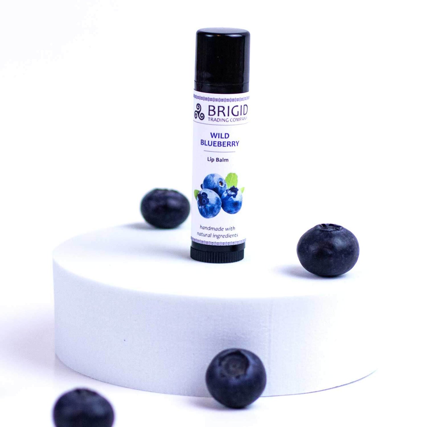 Blueberry natural lip balm tube with black cap, upright, with blueberries nearby.
