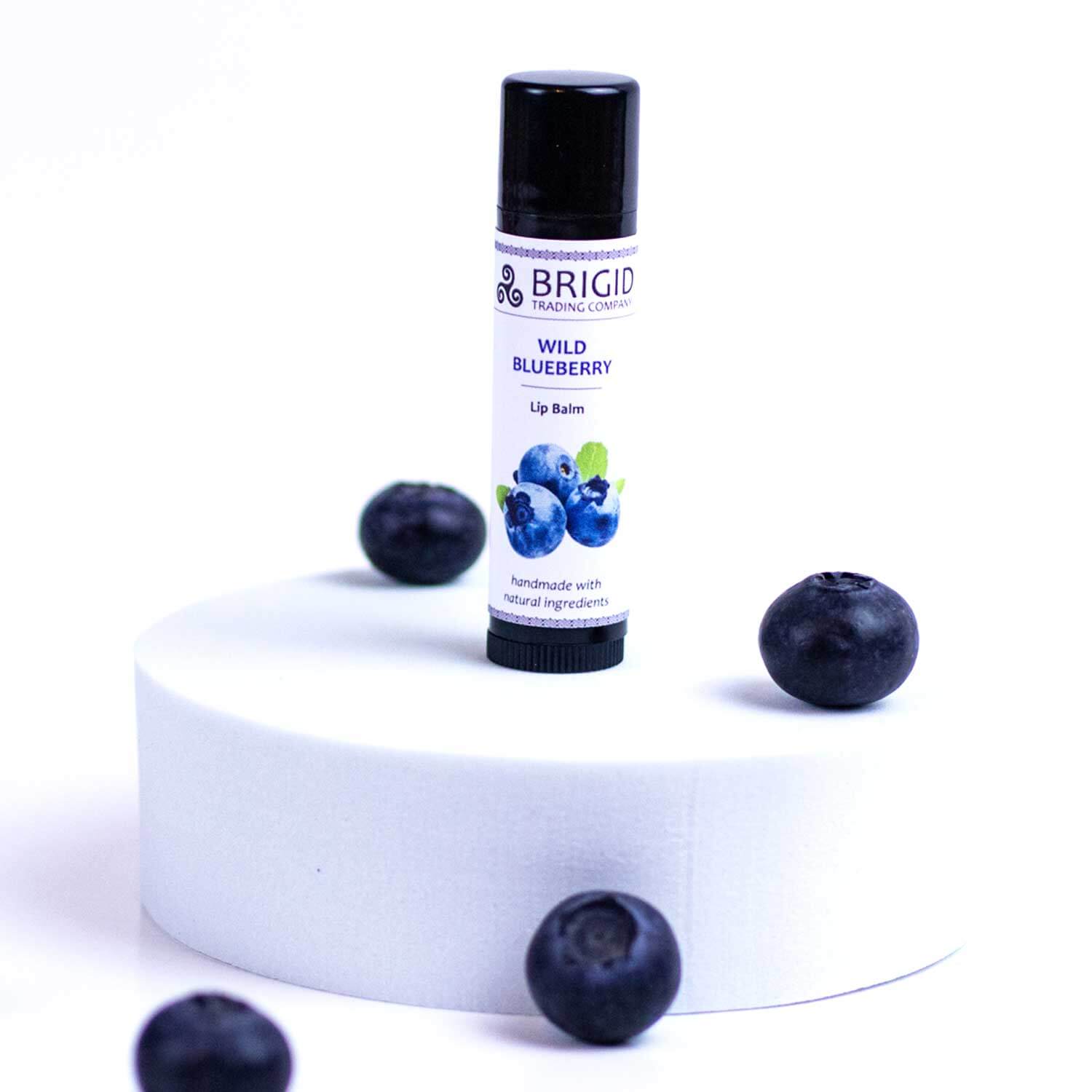Blueberry natural lip balm tube with black cap, upright, with blueberries nearby.