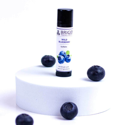Blueberry natural lip balm tube with black cap, upright, with blueberries nearby.