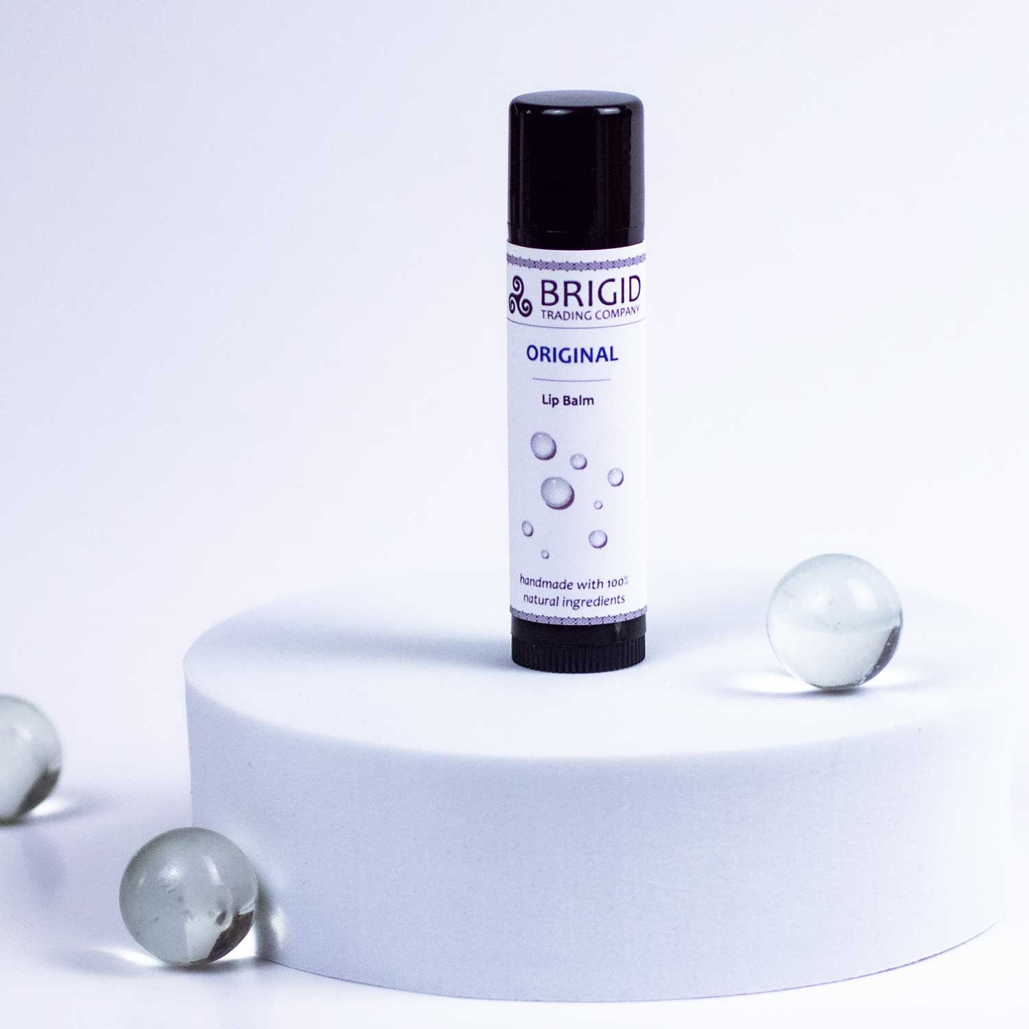 Original natural lip balm tube with black cap and white label on a pedestal