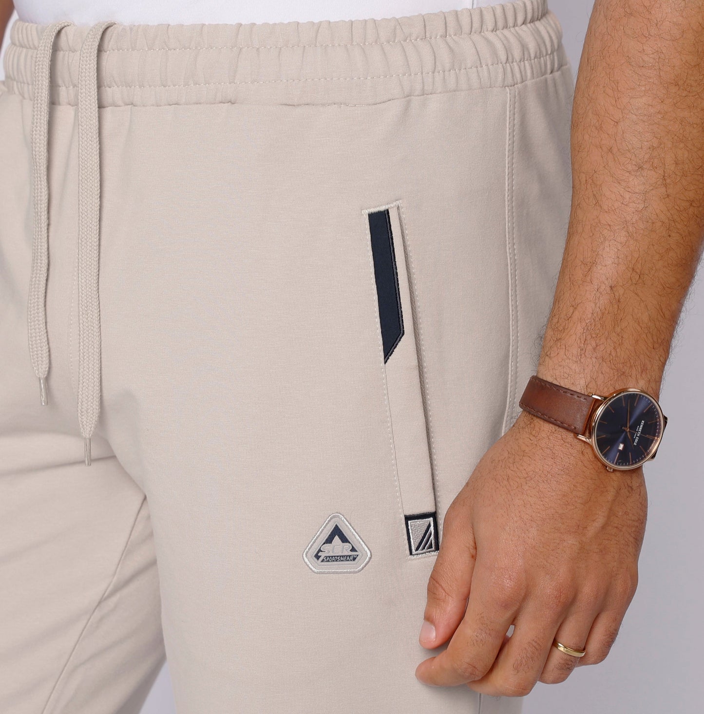 Light beige athletic sweatpants close-up of leg logo patch and drawstring waist