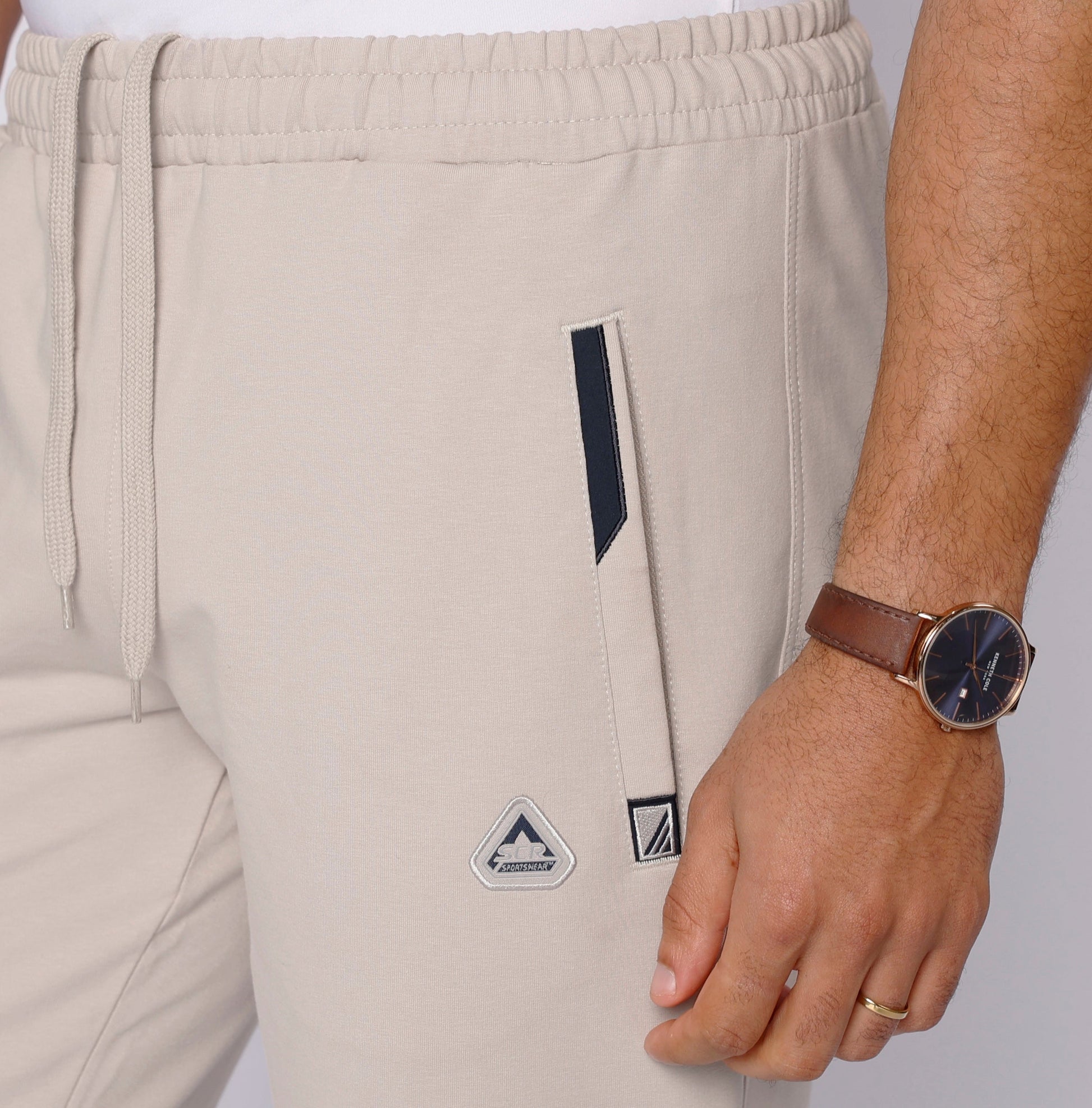 Light beige athletic sweatpants close-up of leg logo patch and drawstring waist