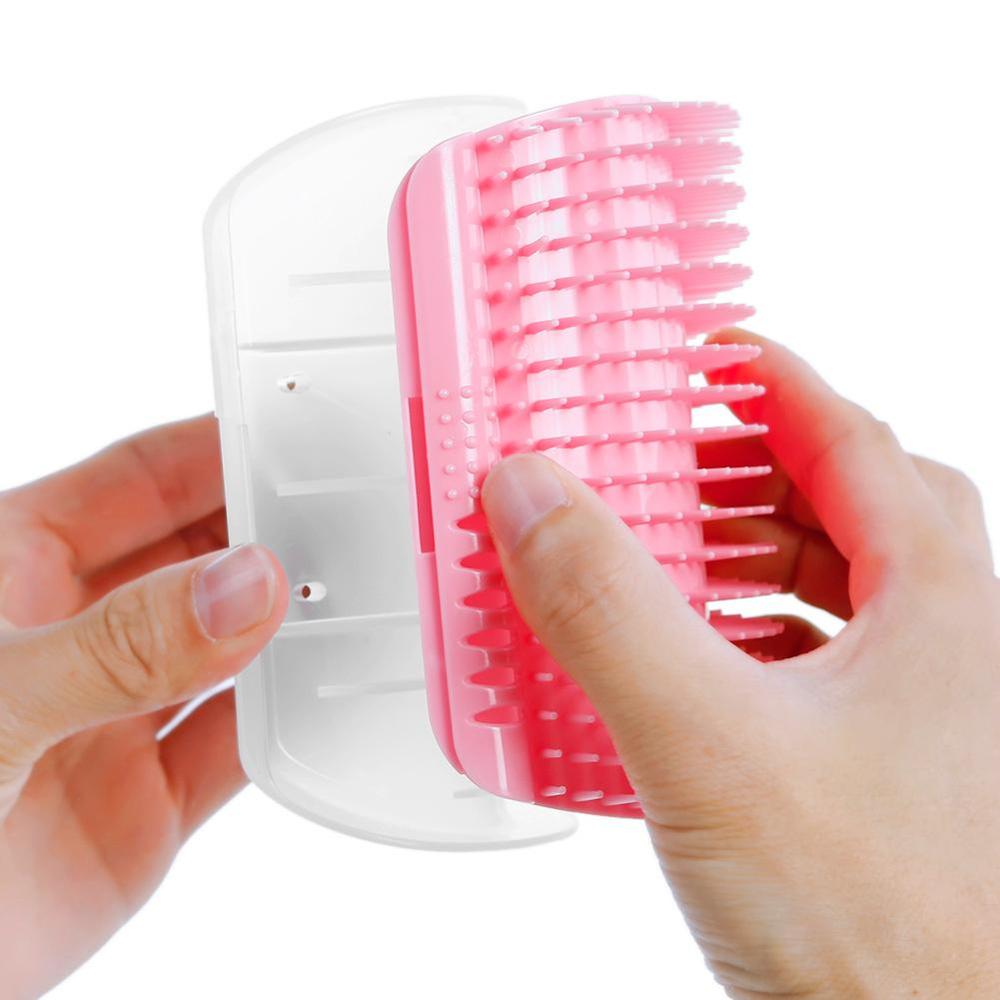 Pink corner grooming brush with dense bristles, held by a hand on a wall mount.