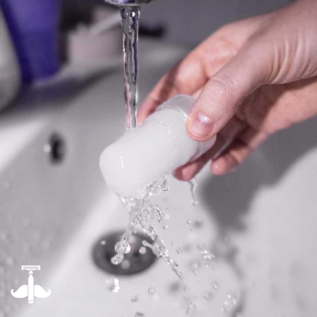 Mineral deodorant stick under running water, with droplets splashing around it