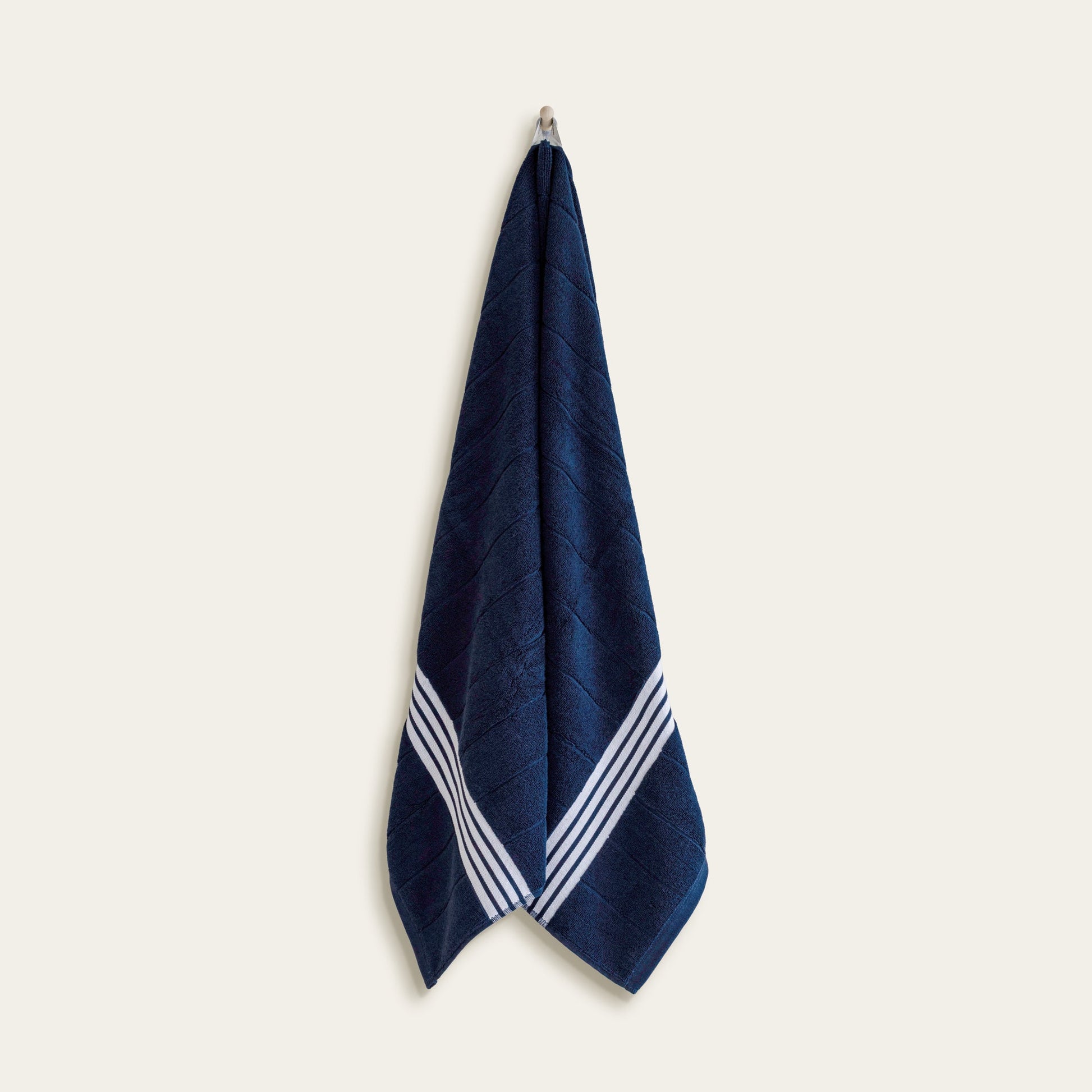 Navy cotton towel with white striped borders, hanging upright view.