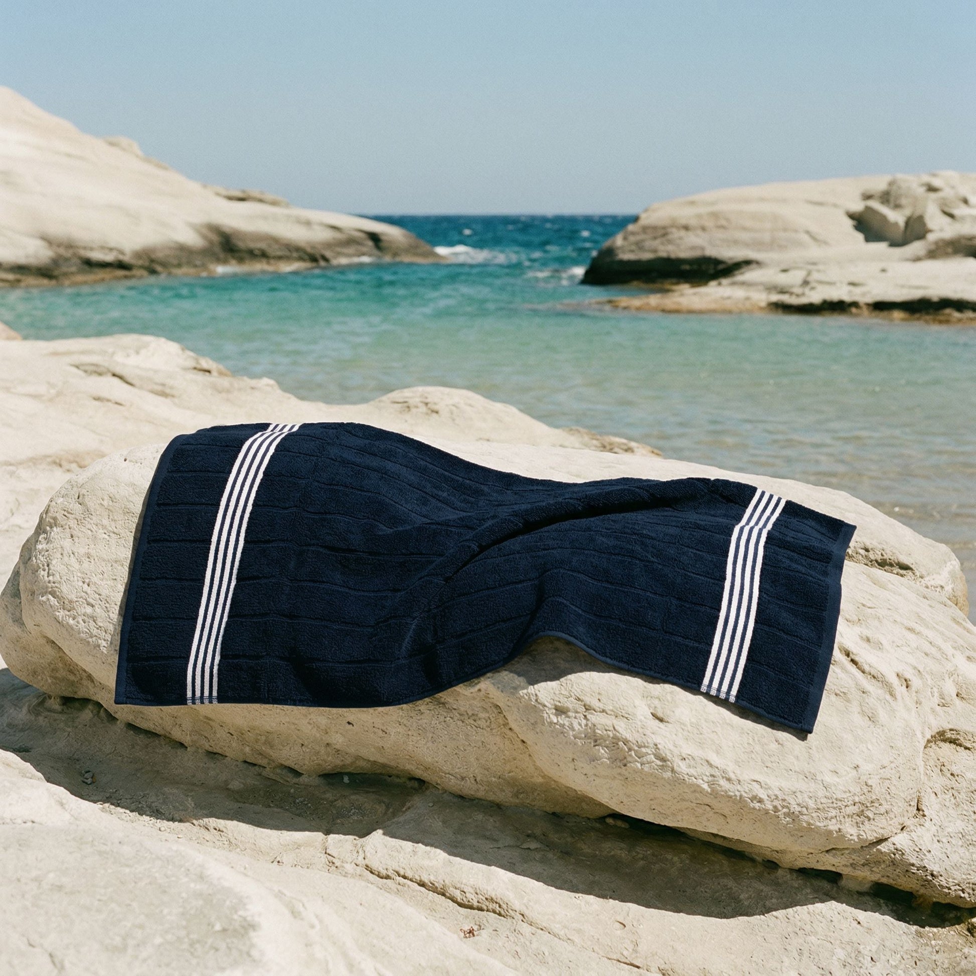 Navy cotton towel with white striped borders, folded on a rock.