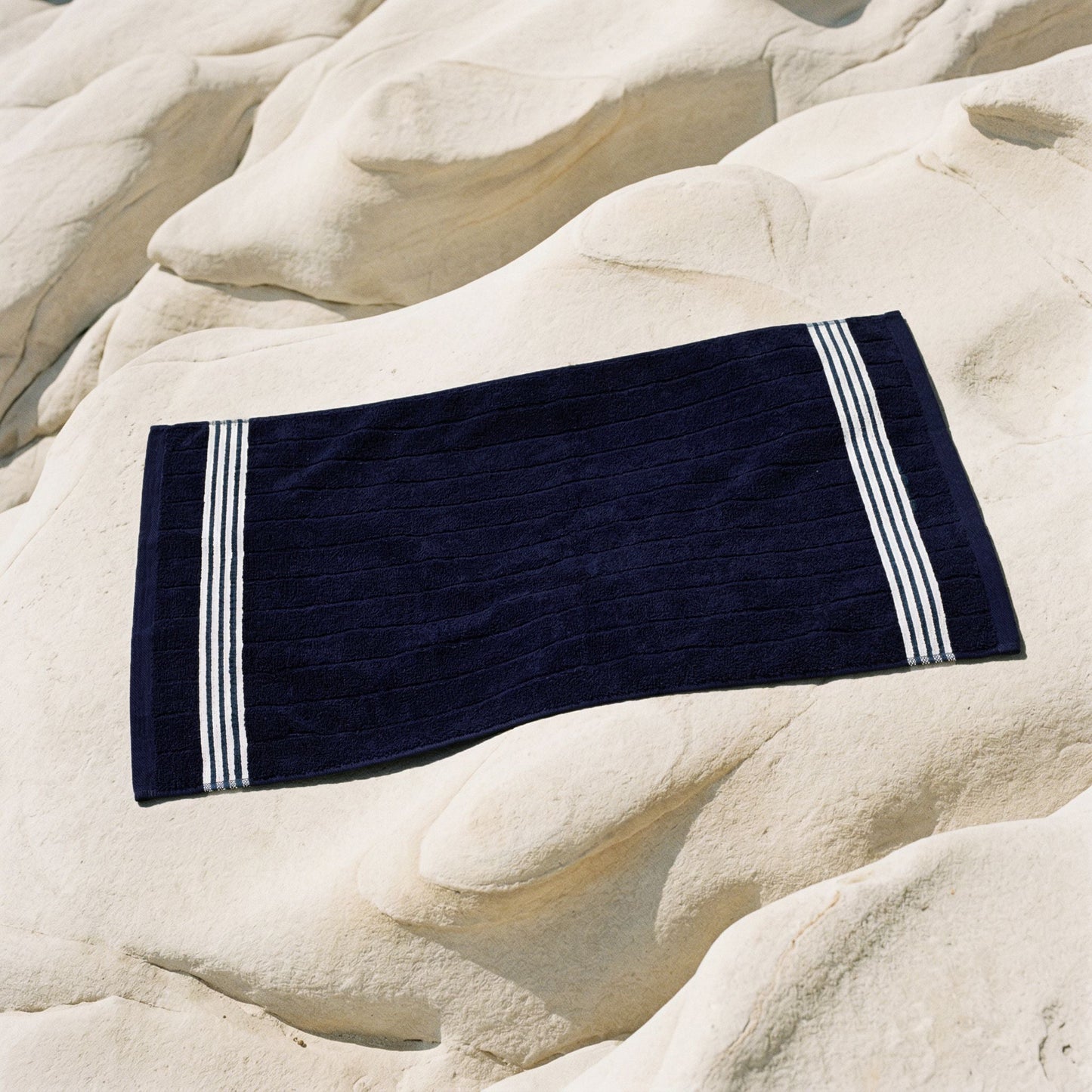 Navy cotton towel with white striped borders, placed on light stone.