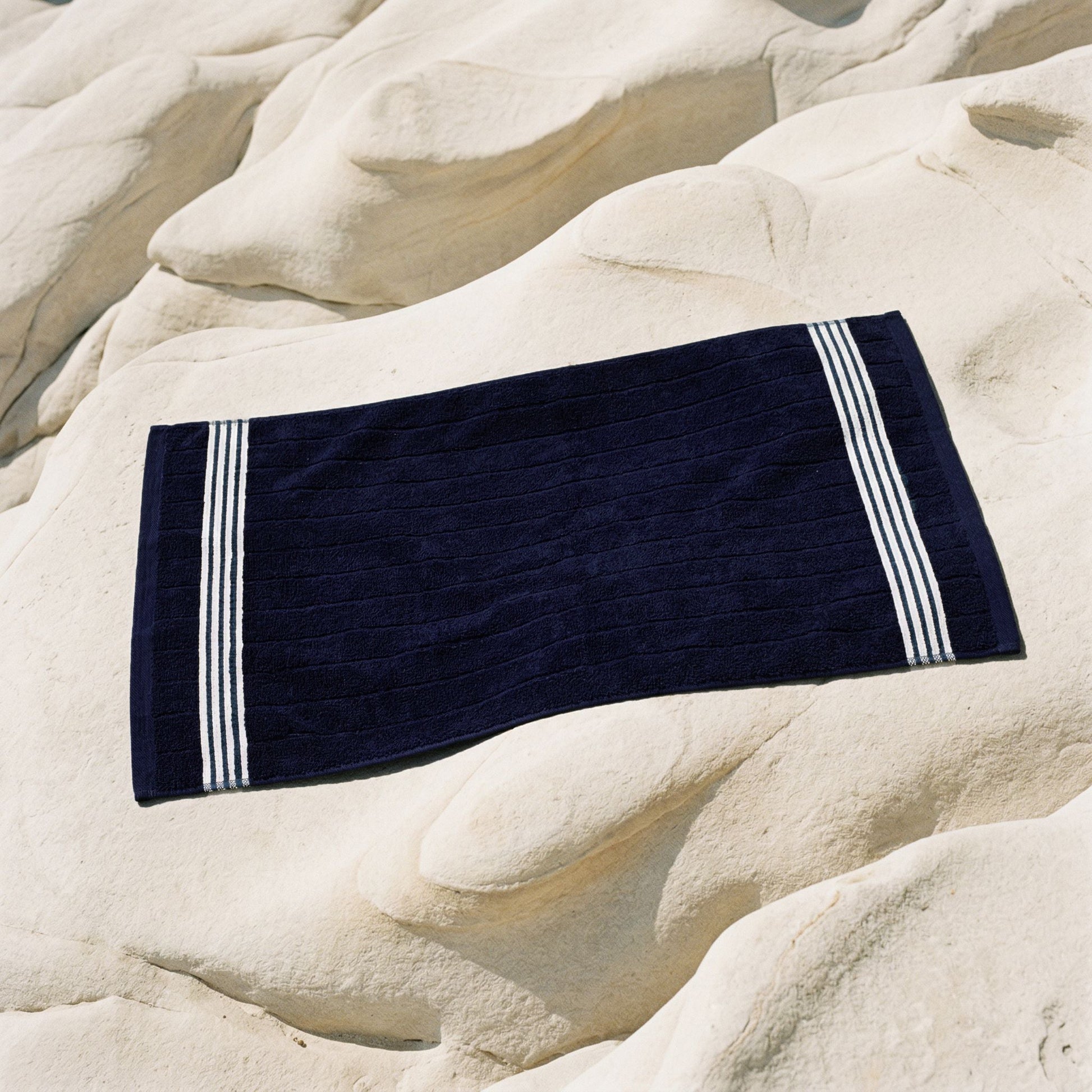 Navy cotton towel with white striped borders, placed on light stone.