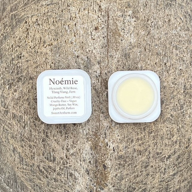 Noémie fragrance balm in small round jar with lid, plus ingredient label card.