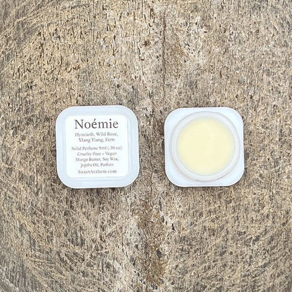 Noémie fragrance balm in small round jar with lid, plus ingredient label card.