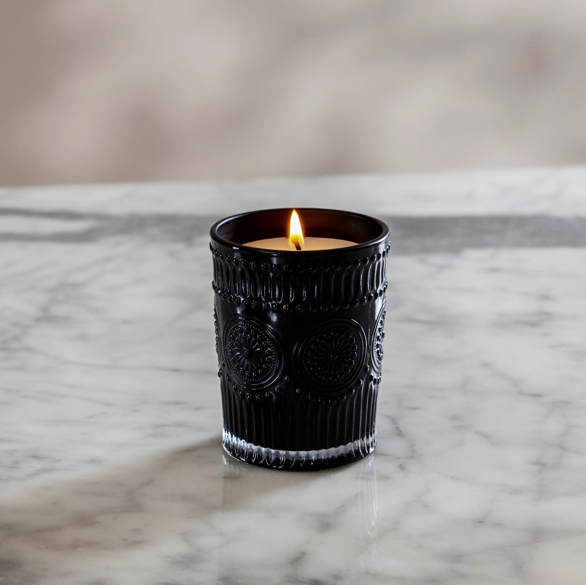 Lit black ribbed glass scented candle with white wax and flame