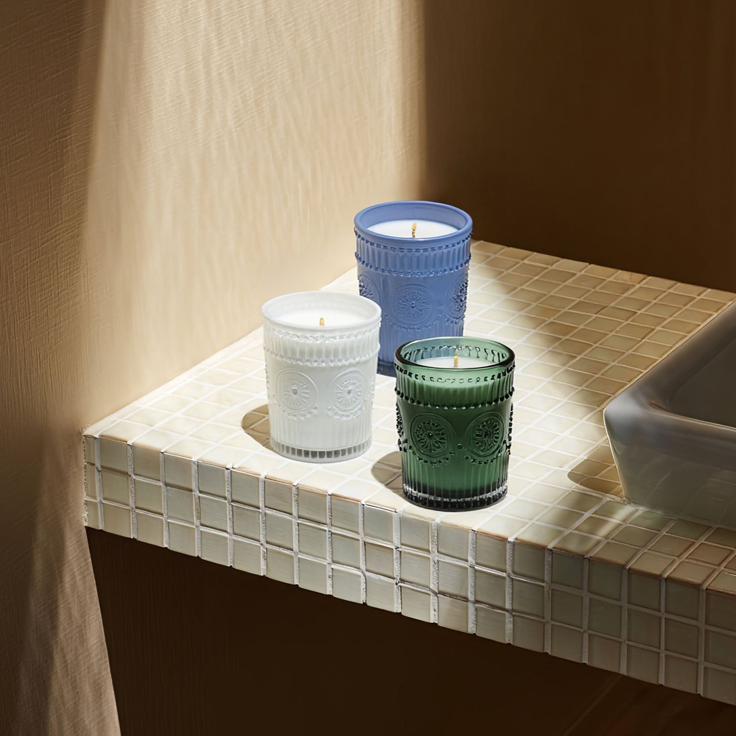 Scented glass candles with white, blue, and green jars on a tiled shelf