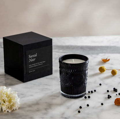 Santal Noir gift box next to dark ribbed glass candle with white wax and steady wick