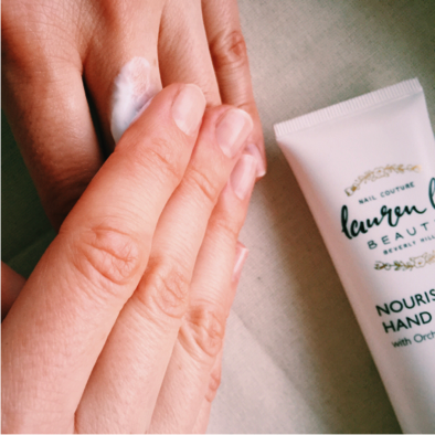 Hand applying white cream with Laura b. hand cream tube nearby