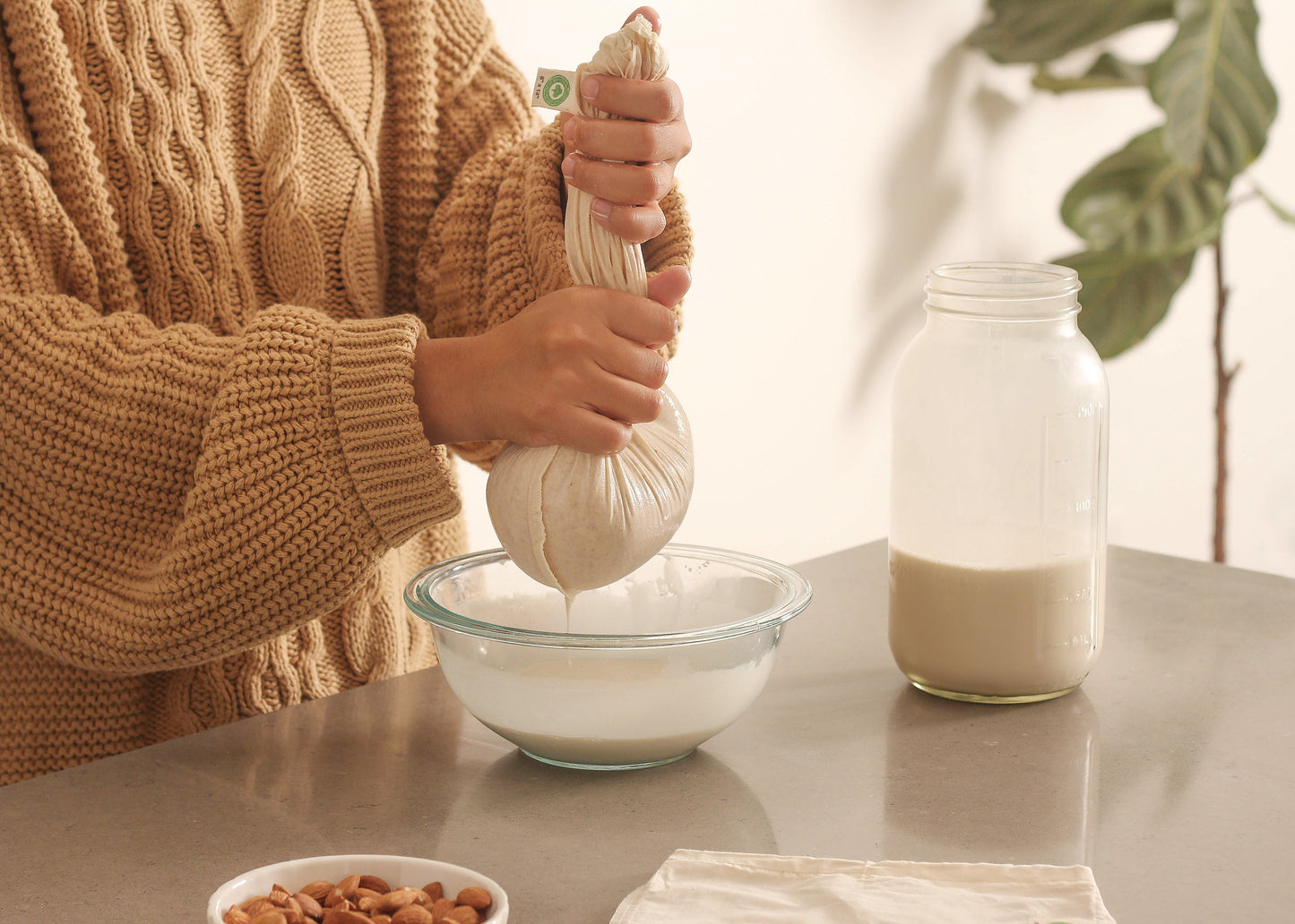 Nut milk bag being filled, off-white mesh pouch with rope drawstring