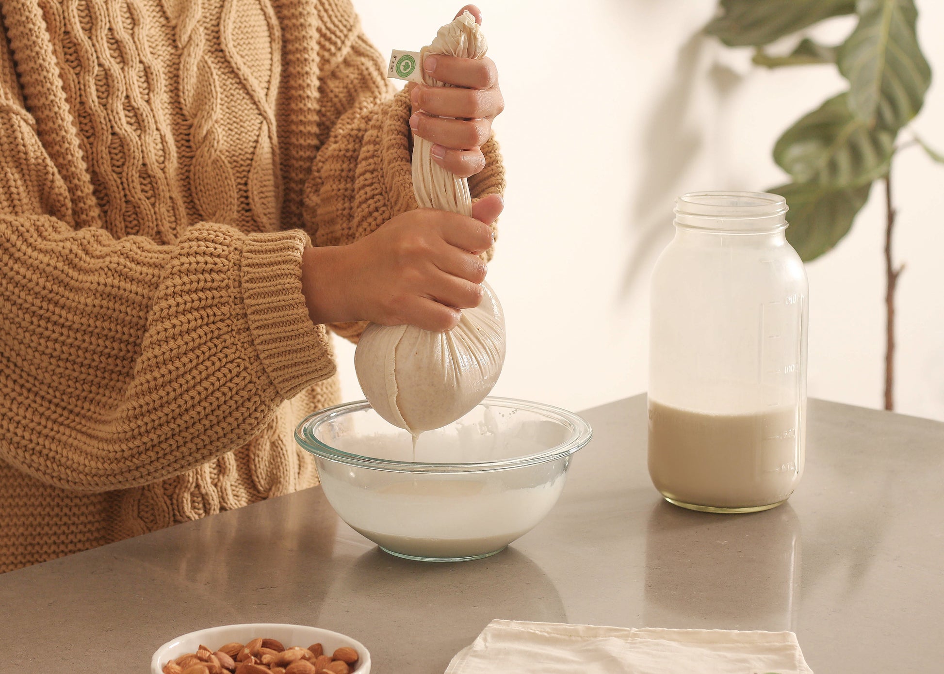 Nut milk bag being filled, off-white mesh pouch with rope drawstring