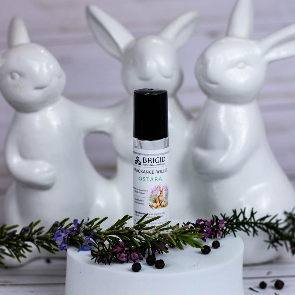 Ostara fragrance roller with black cap on a white stand, with small herbs on top