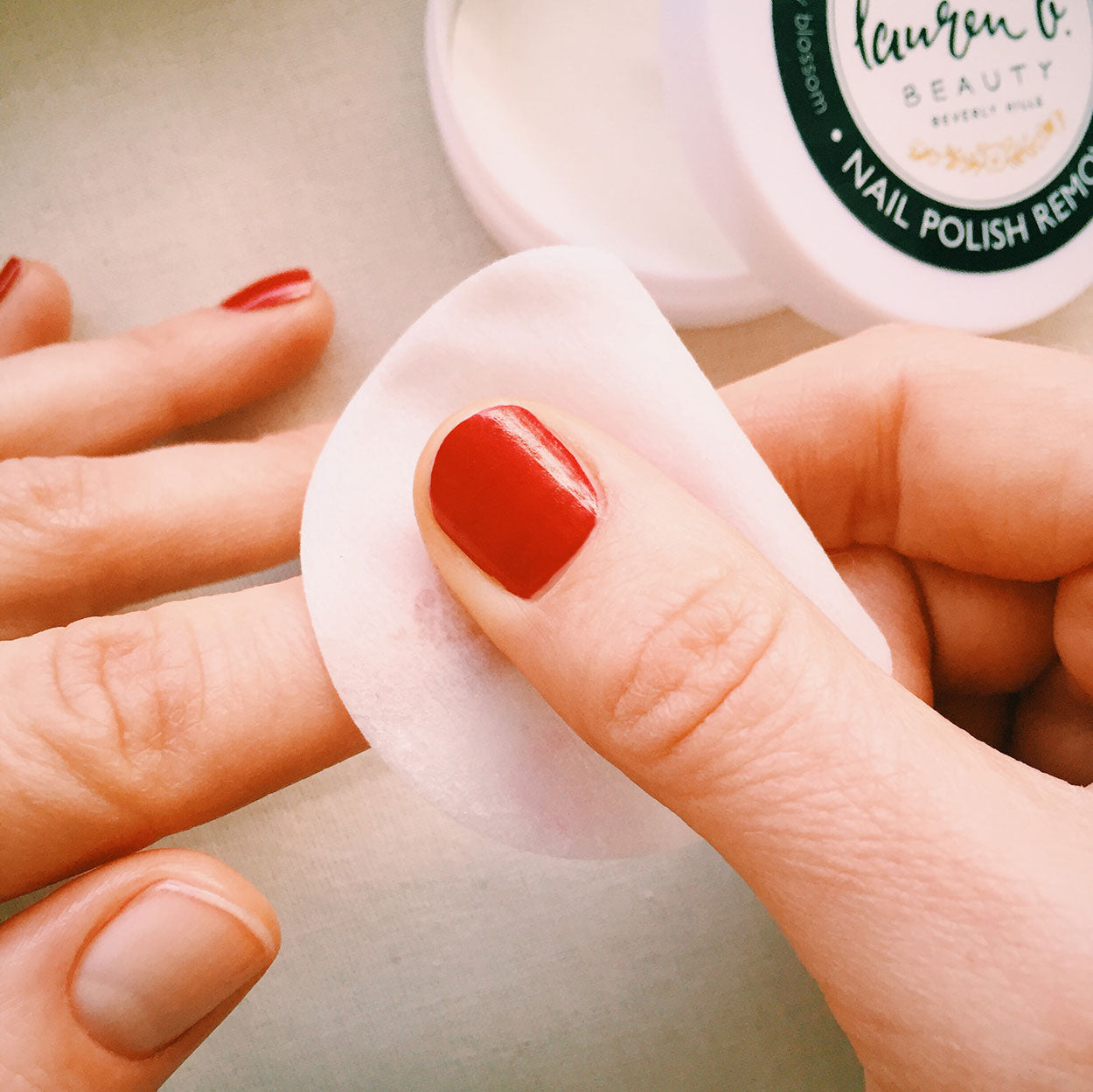 Nail polish remover pad against fingers with red nail polish