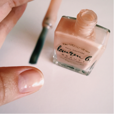 Nail base coat being applied on nails with nude peach bottle and brush.
