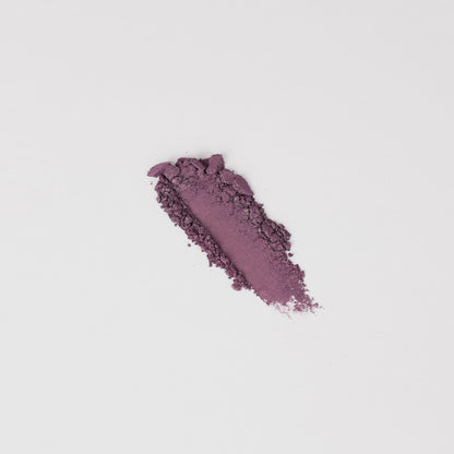 Pressed eyeshadow swatch in soft purple shimmer with scattered powder bits