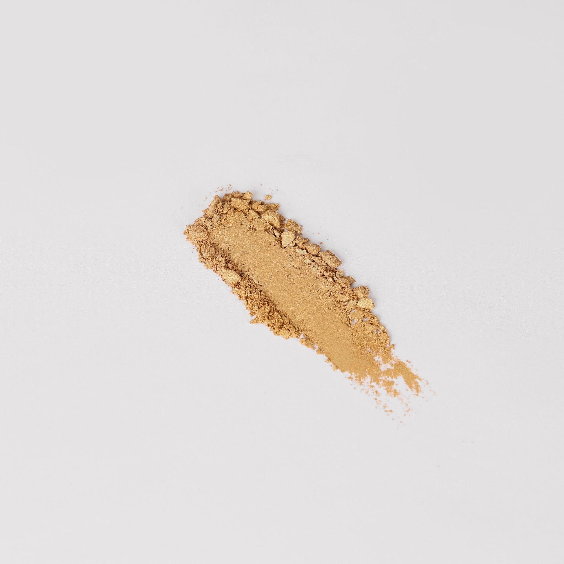Pressed eyeshadow swatch in light gold-beige shimmer on skin-like surface