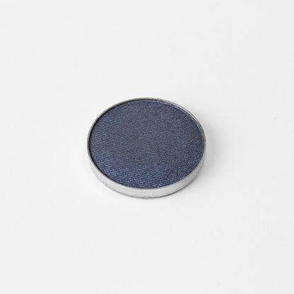 Pressed eyeshadow pan with dark navy-blue shimmer powder and silver rim.