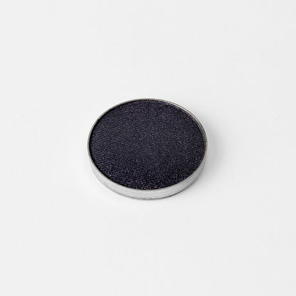 Pressed eyeshadow pan with deep blue-gray shimmer finish and silver rim.