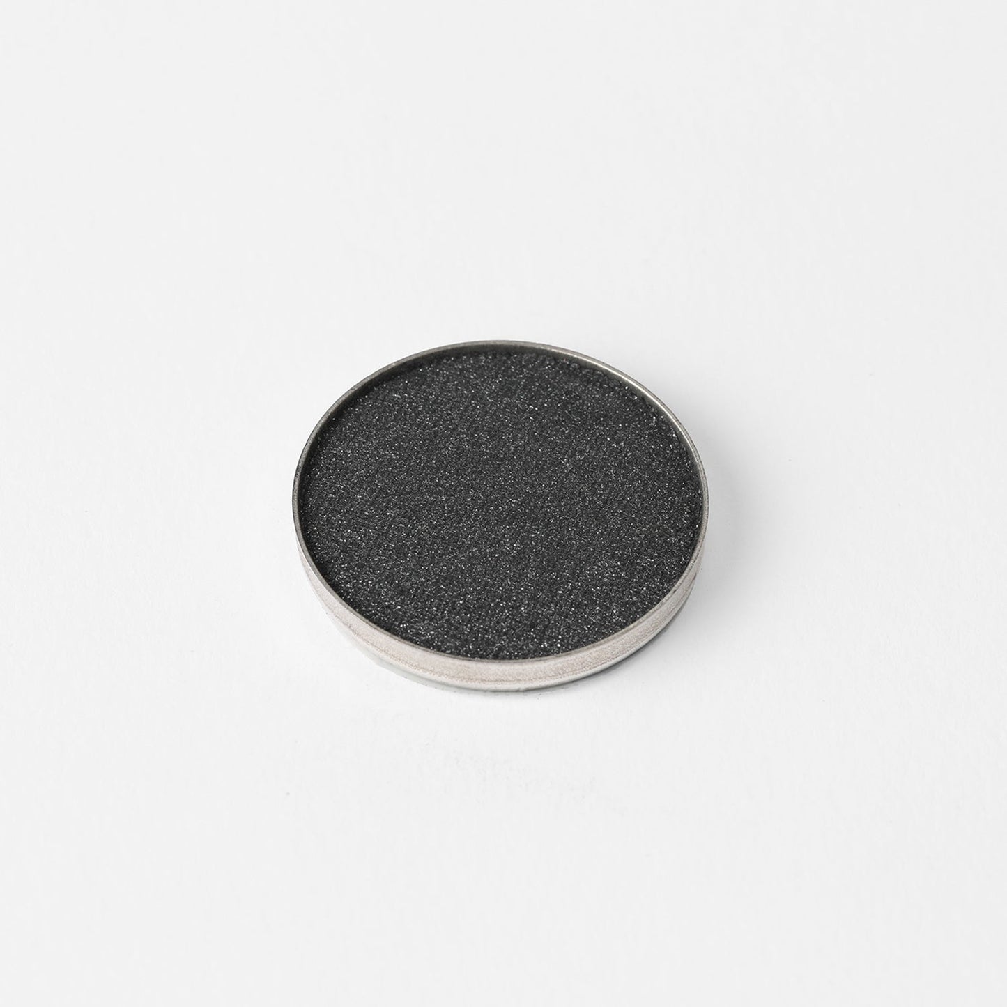Pressed eyeshadow pan with blackish charcoal shimmer powder and silver rim.