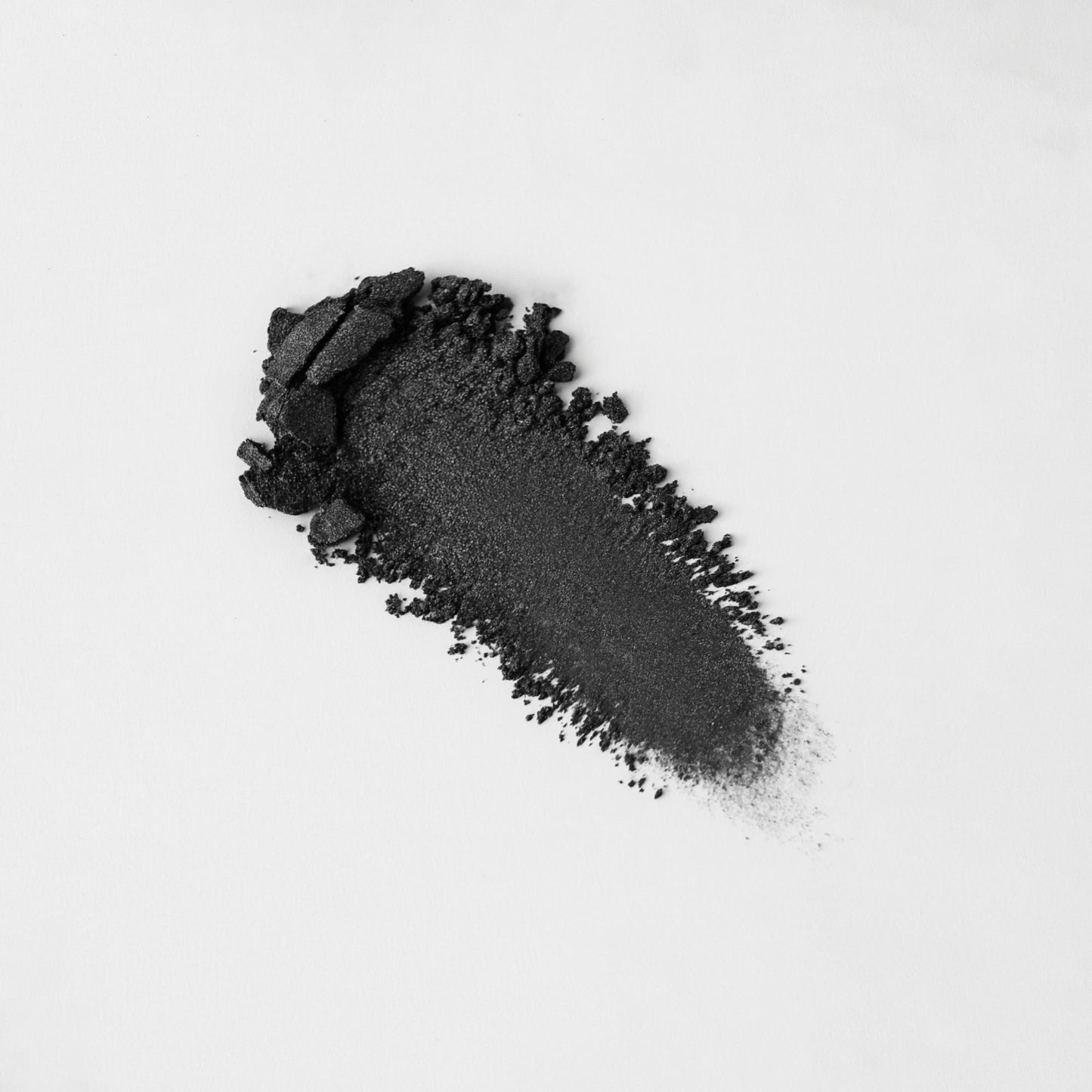 Pressed eyeshadow swatch, deep charcoal black shimmer with crumbly powder texture.