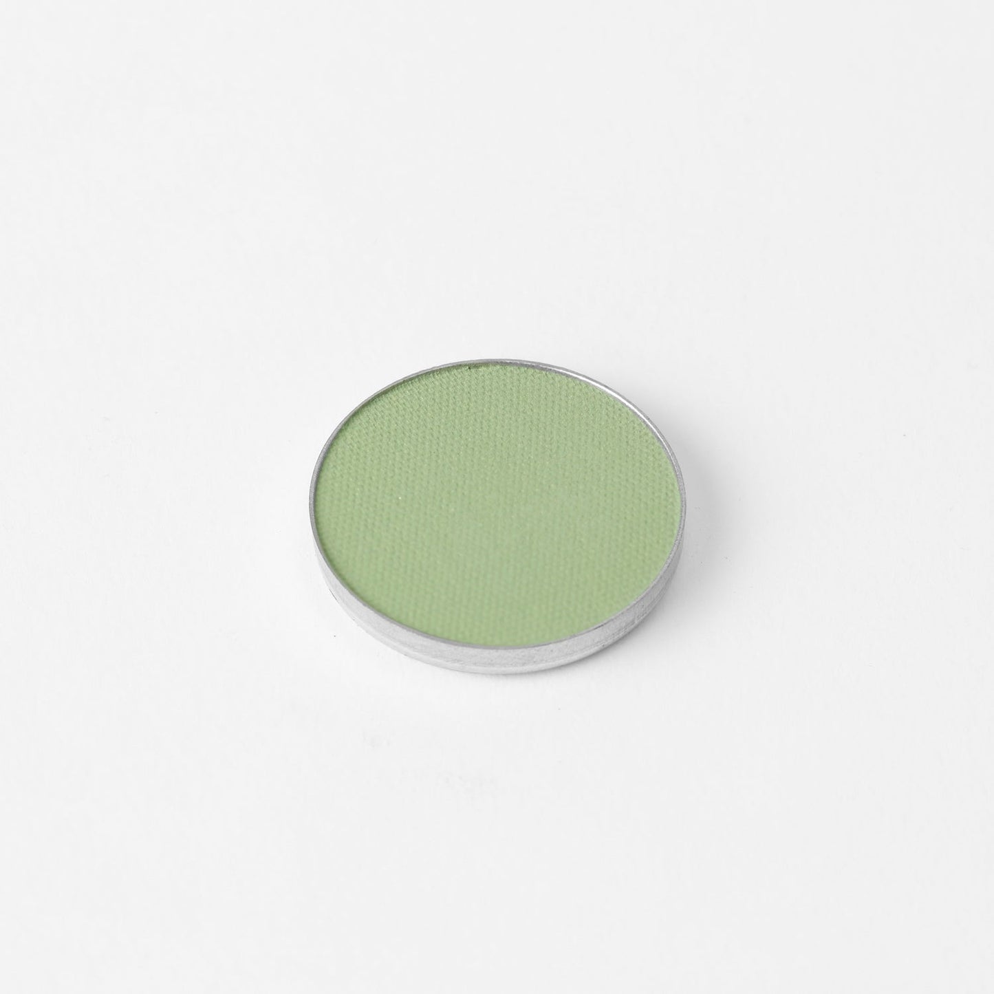 Pressed eyeshadow pan with soft pale green shade in a round compact.