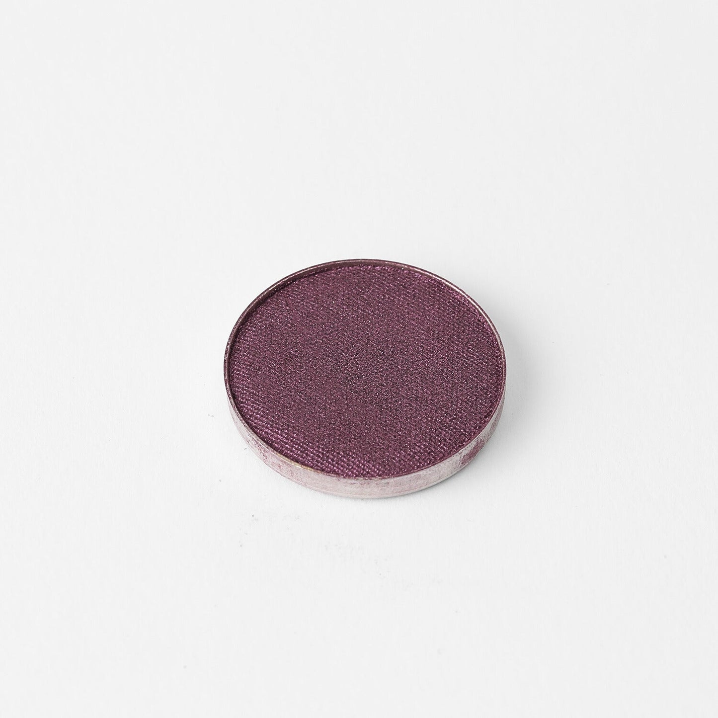 Pressed eyeshadow pan with shimmering plum-purple color