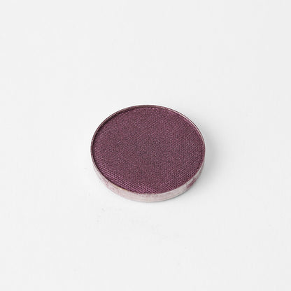 Pressed eyeshadow pan with shimmering plum-purple color