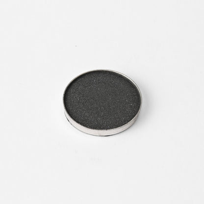 Round pressed eyeshadow pan with dark charcoal shimmer finish