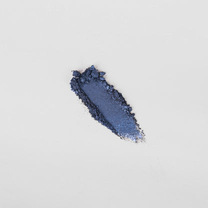 Pressed eyeshadow swatch, dark blue shimmer powder with glittery edges.