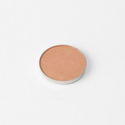 Pressed eyeshadow pan with warm apricot shimmer finish, round compact.