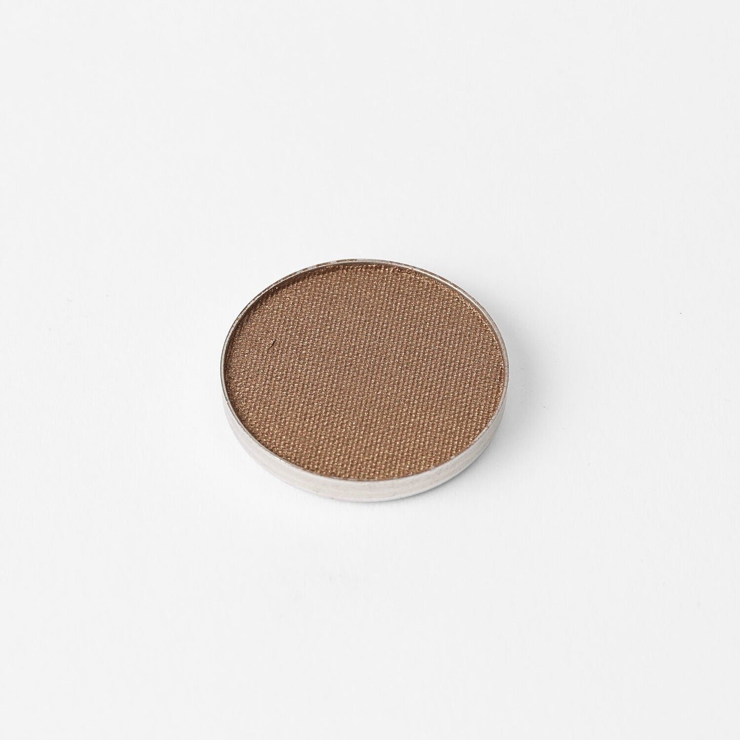 Pressed eyeshadow pan with matte bronze-tan shade in a round compact.
