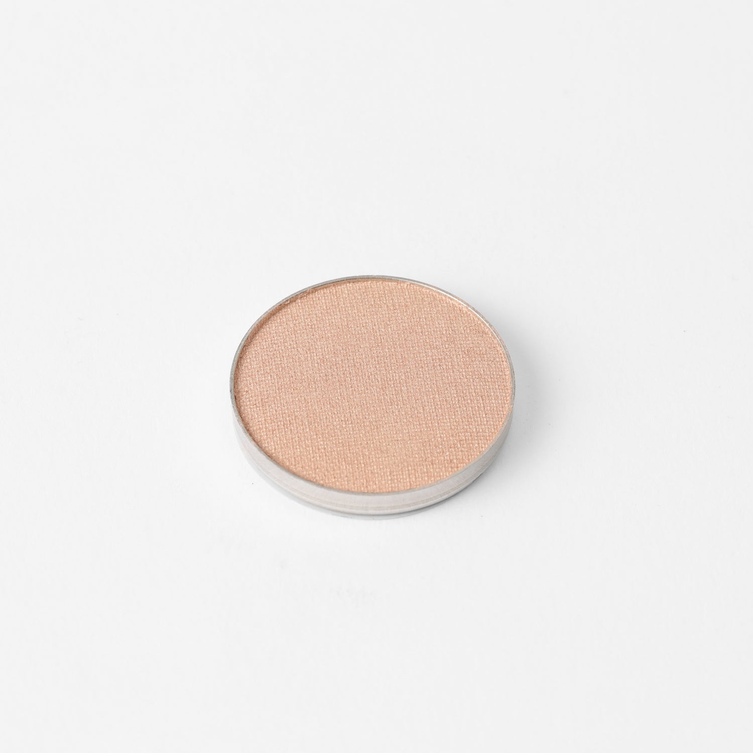 Pressed eyeshadow pan with warm peach shimmer finish, round compact.